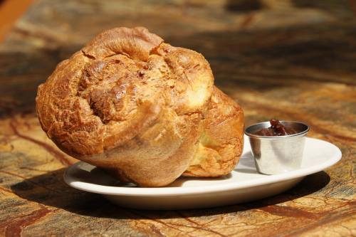 A golden-brown popover on a white plate, accompanied by a small cup of dark sauce.
