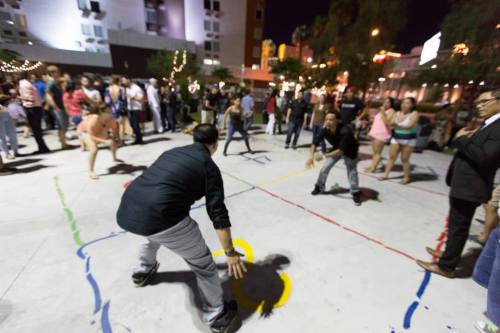 A lively outdoor scene at night with people dancing and playing games on a colorful marked pavement.