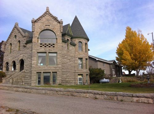 A large, stone castle-like house with a turret, surrounded by trees and a driveway.