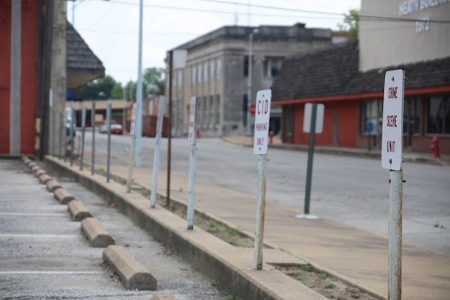A row of weathered signs along an empty street, indicating parking restrictions and a crime scene unit.