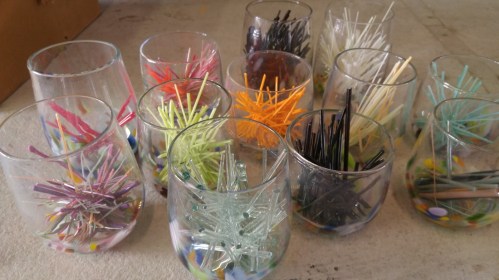 A collection of glasses filled with colorful, decorative sticks arranged in various patterns.