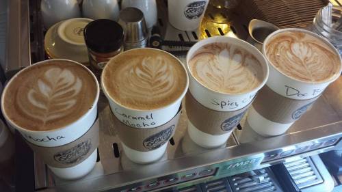 Four coffee cups with latte art, labeled Mocha, Caramel Mocha, Spicy Chai, and Doc B, on a counter.