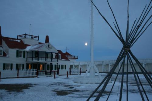 Historic building with a red roof, a teepee, and a full moon in a snowy landscape at dusk.