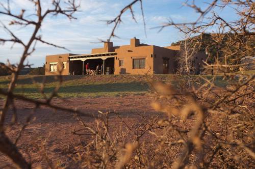 A southwestern-style adobe house surrounded by sparse vegetation, set against a clear sky at sunset.