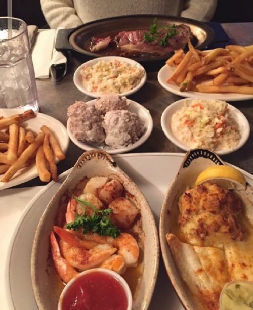A table set with a variety of dishes, including shrimp, fish, fries, coleslaw, and rolls, alongside a glass of water.