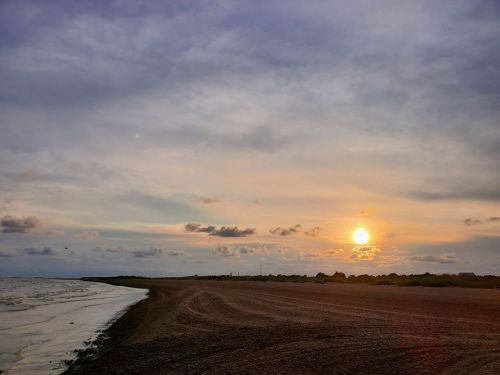 A serene beach at sunset, with gentle waves and a colorful sky filled with clouds.