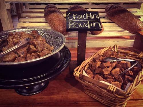 A display of food featuring a silver platter of boudin and a basket of crispy bread cubes, with loaves in the background.