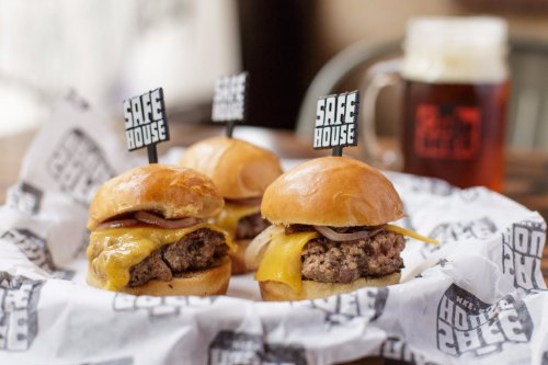 Three mini cheeseburgers with melted cheese and onions, served on a platter with a beer in the background.