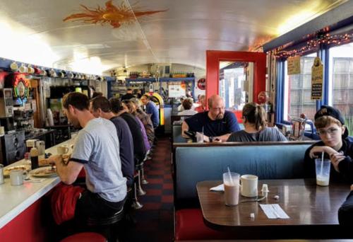 A bustling diner interior with patrons enjoying meals at booths and a counter, colorful decor, and a cozy atmosphere.