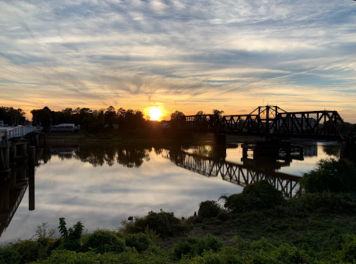 Sunset over a river with a bridge silhouetted against the colorful sky, reflecting on the water's surface.