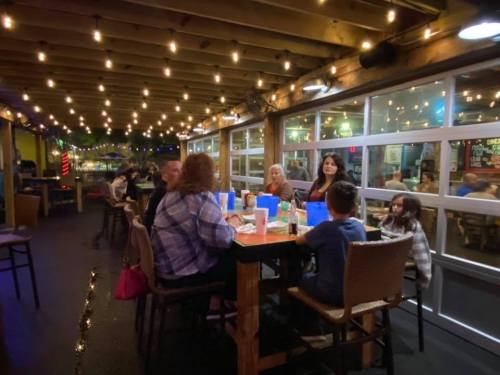 A group of people dining at a restaurant with string lights overhead, enjoying a lively evening together.