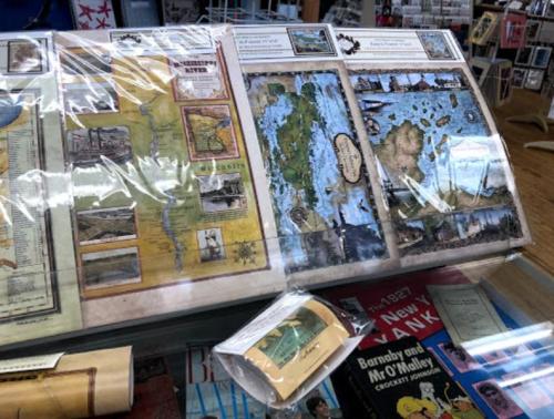 A display of vintage maps, including a river map and a detailed island map, under protective plastic in a shop.