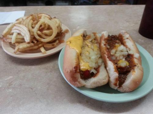 Two chili cheese hot dogs topped with onions on a green plate, alongside a plate of curly fries.