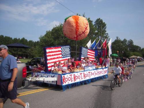 A festive parade float decorated with flags and a large baseball, featuring children and adults celebrating.