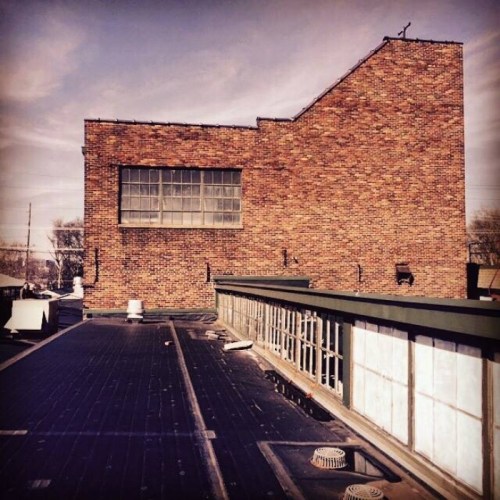 A rooftop view featuring a brick building and flat roof with ventilation units under a clear sky.