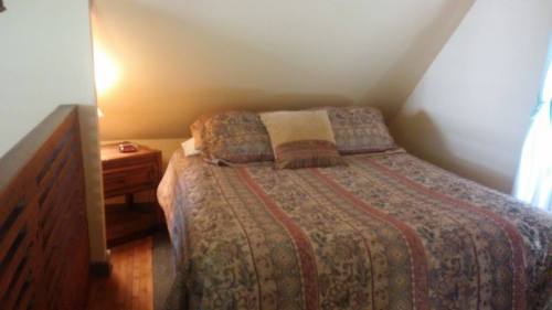 Cozy bedroom with a patterned bedspread, a nightstand, and a lamp, featuring sloped walls and warm lighting.