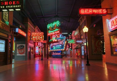 A vibrant indoor street scene with colorful neon signs for restaurants and shops, creating a lively atmosphere.