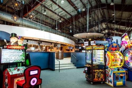 Bright arcade area featuring games like Monopoly and a variety of colorful machines in a spacious, modern setting.