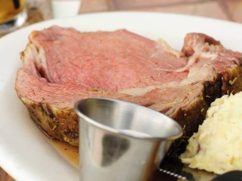 A plate featuring a large slice of roast beef with a small metal cup and a side of mashed potatoes.