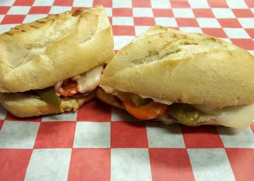 Two sandwiches filled with meats, cheese, and colorful peppers, resting on a red and white checkered tablecloth.