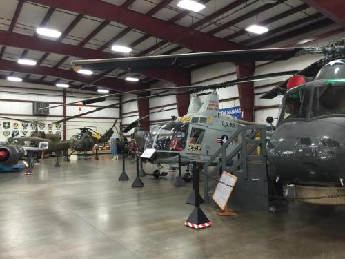 A display of military helicopters inside a hangar, with various aircraft and insignia on the walls.