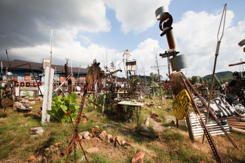 A whimsical outdoor art installation featuring various metal sculptures and structures amidst grassy terrain under a cloudy sky.
