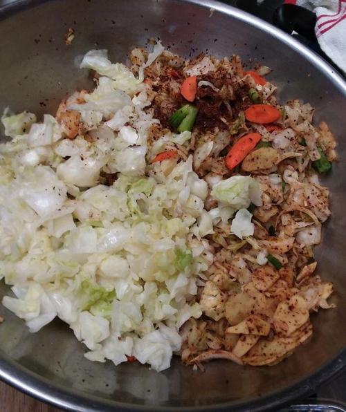A large bowl filled with chopped cabbage, carrots, and spices, ready for mixing or cooking.