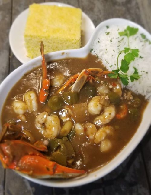 A bowl of shrimp and crab gumbo with rice and a slice of cornbread on the side, garnished with cilantro.