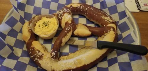 A large pretzel with coarse salt, served with a side of creamy dip on a blue and white checkered tray.