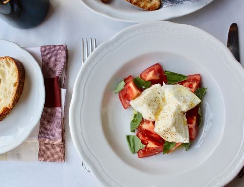 A white plate with fresh tomatoes, basil, and mozzarella balls, garnished with seasoning, on a table setting.