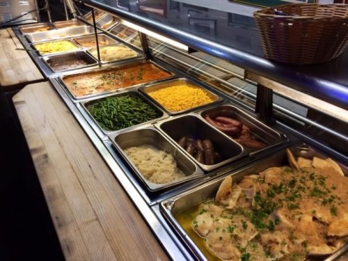 A buffet line featuring various dishes, including meats, vegetables, and sides in metal trays.