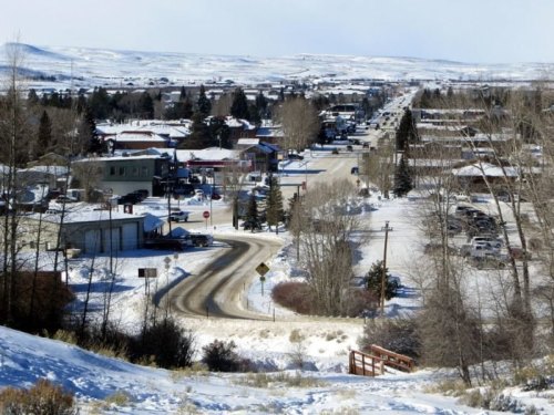 A snowy landscape showing a small town with streets, buildings, and trees under a clear blue sky.