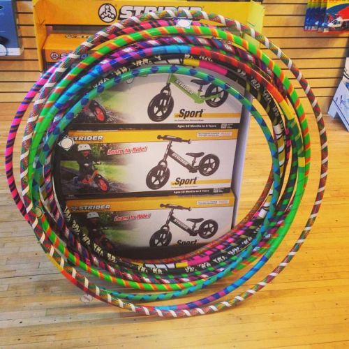 A stack of colorful hula hoops in front of boxes for Strider balance bikes in a store display.