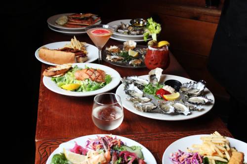A table with various seafood dishes, including oysters, shrimp, a cocktail, and a hot dog, alongside a glass of water.
