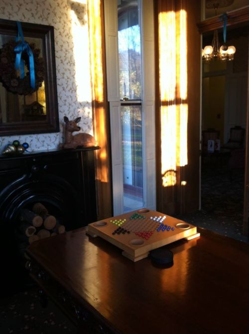 A cozy room with sunlight streaming in, featuring a game board on a table and a decorative wreath on the wall.