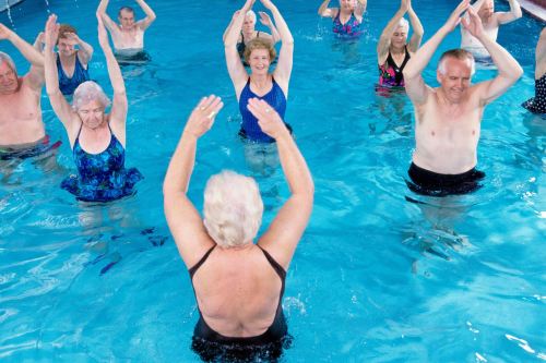 A group of seniors participating in a water aerobics class, raising their arms in a pool.