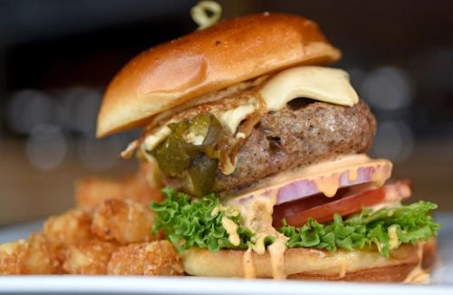 A juicy burger with cheese, jalapeños, lettuce, tomato, and special sauce, served with crispy tater tots on the side.