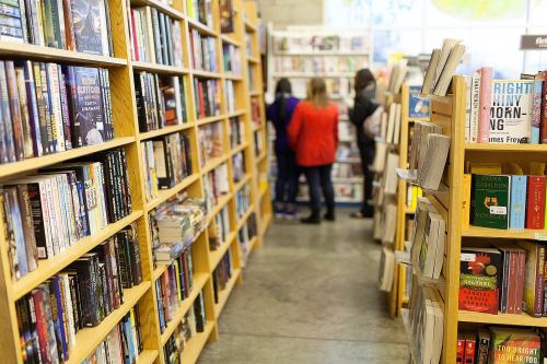 A cozy bookstore aisle lined with bookshelves, with customers browsing in the background.