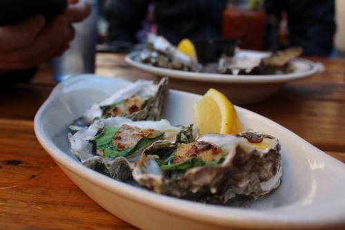 A plate of grilled oysters topped with herbs and a lemon wedge, served on a wooden table.