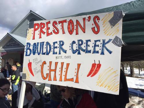 Sign for "Preston's Boulder Creek Chili" at an outdoor event in Boise, Idaho, with colorful lettering and chili pepper illustrations.