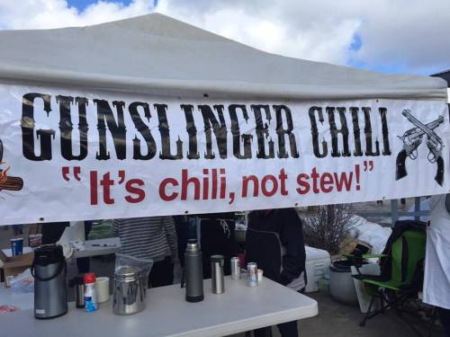 A banner reading "Gunslinger Chili" with the tagline "It's chili, not stew!" displayed at a food event.