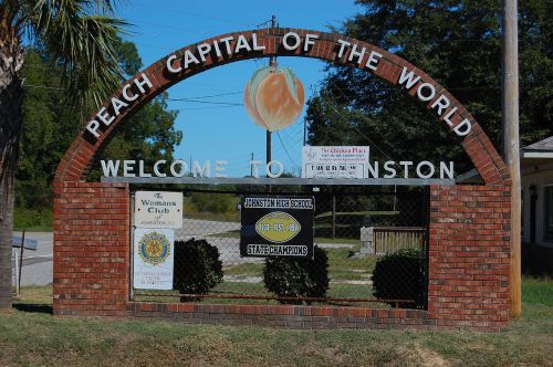 Sign welcoming visitors to Johnston, SC, known as the "Peach Capital of the World," featuring local achievements.