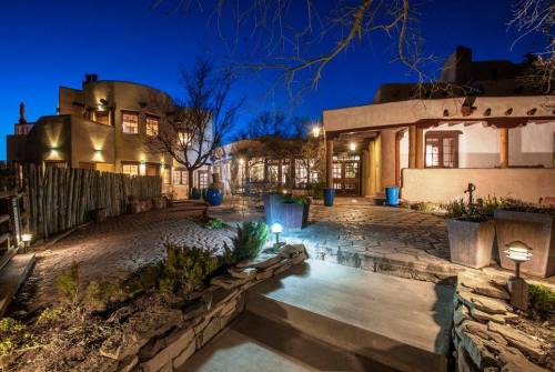 A beautifully lit outdoor area of a southwestern-style building at dusk, featuring stone pathways and potted plants.
