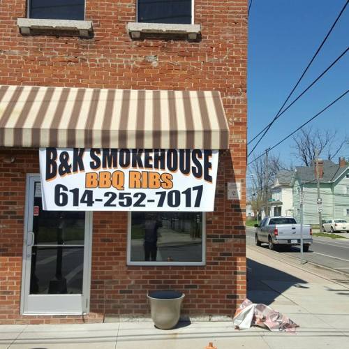 A brick building with a striped awning and a large sign for B&K Smokehouse BBQ Ribs, featuring a phone number.