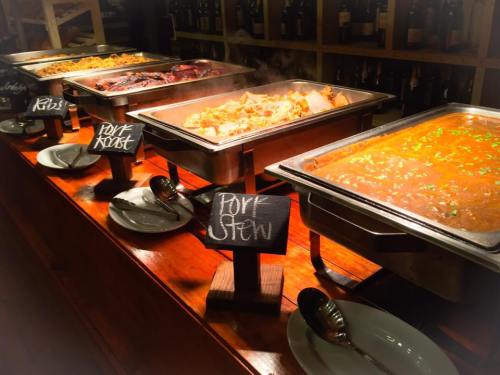 A buffet table featuring various pork dishes, including pork roast and pork stew, with chalkboard labels.