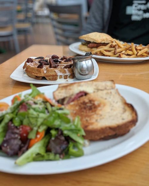 A table with a sandwich, salad, and a plate of fries, alongside a dessert topped with nuts.