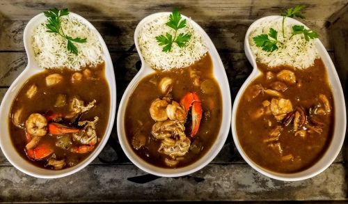 Three bowls of gumbo with shrimp and chicken, served with white rice and garnished with fresh parsley.
