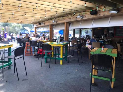 Outdoor dining area with colorful tables and chairs, string lights overhead, and people enjoying their meals.