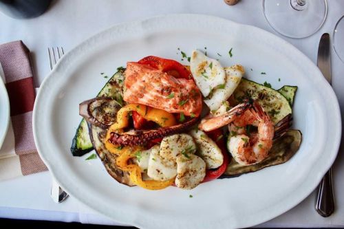 A platter of grilled seafood including shrimp, salmon, and octopus, served with colorful roasted vegetables.