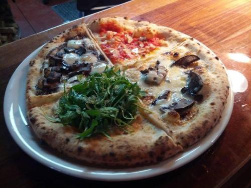 A round pizza divided into four sections, featuring various toppings like mushrooms, cheese, tomato, and arugula.